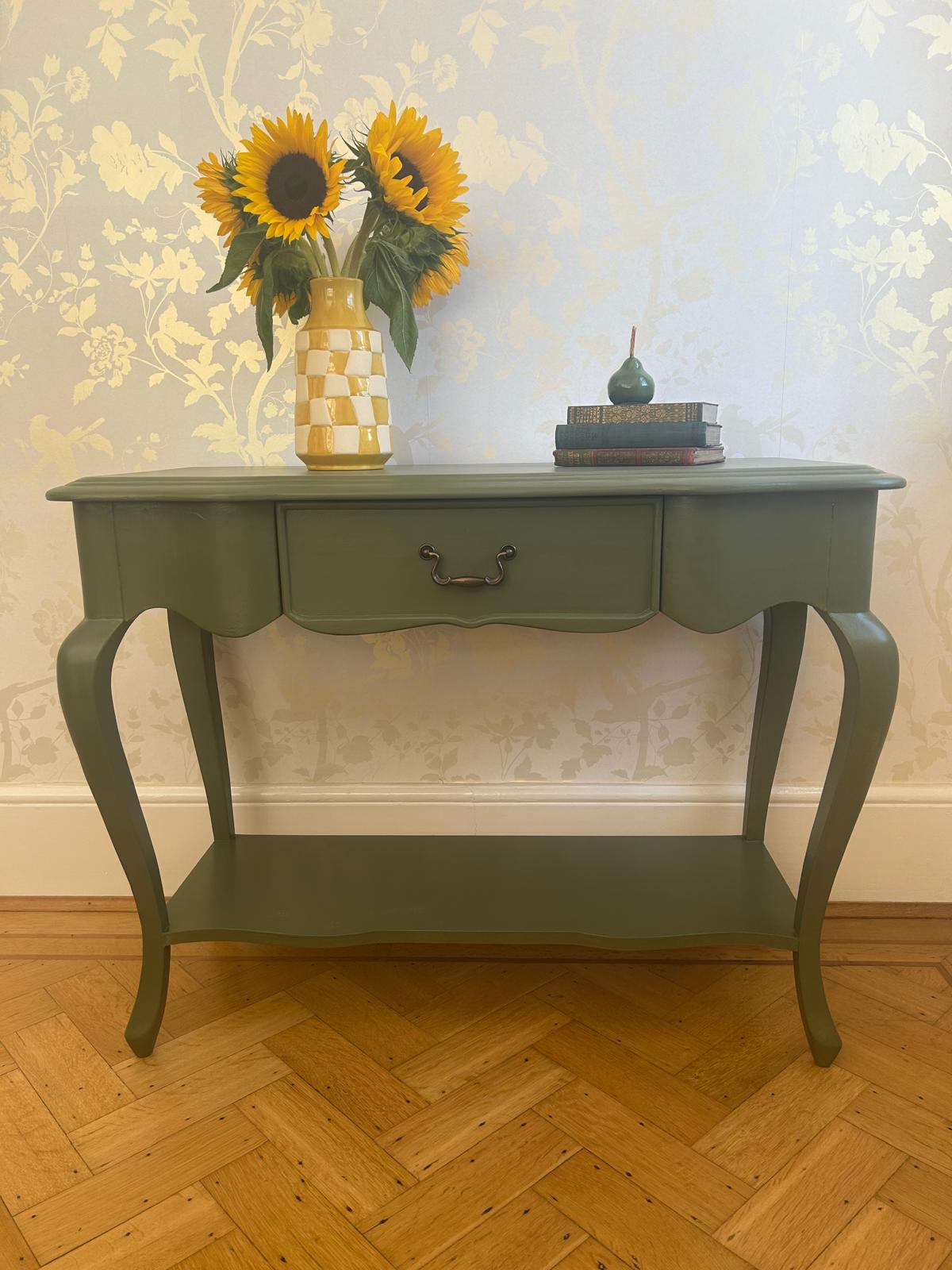olive green console table with vase of sunflowers and books.